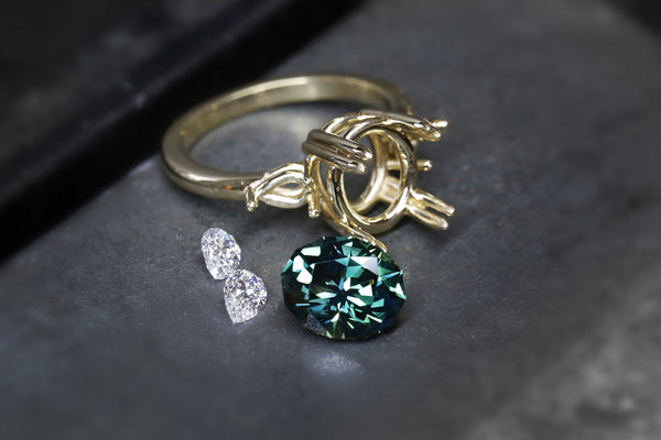 loose Australian sapphire and white diamonds with gold setting on a jeweller bench.