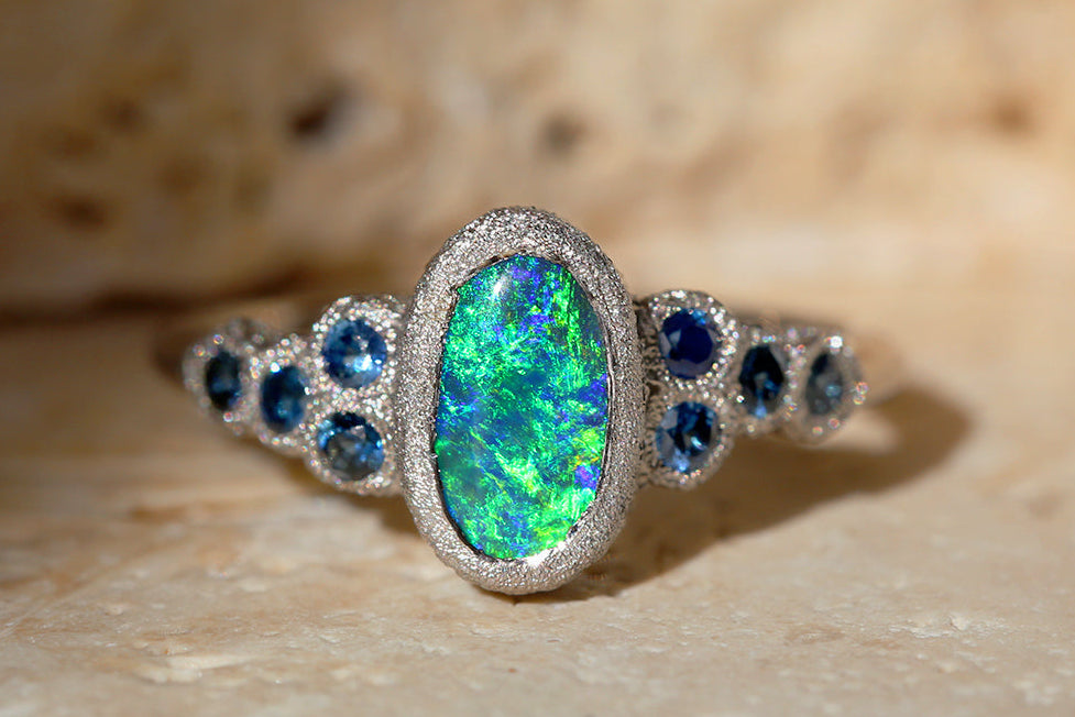 Ring with a oceanic colour Australian black opal and blue gemstones on a beige stone background