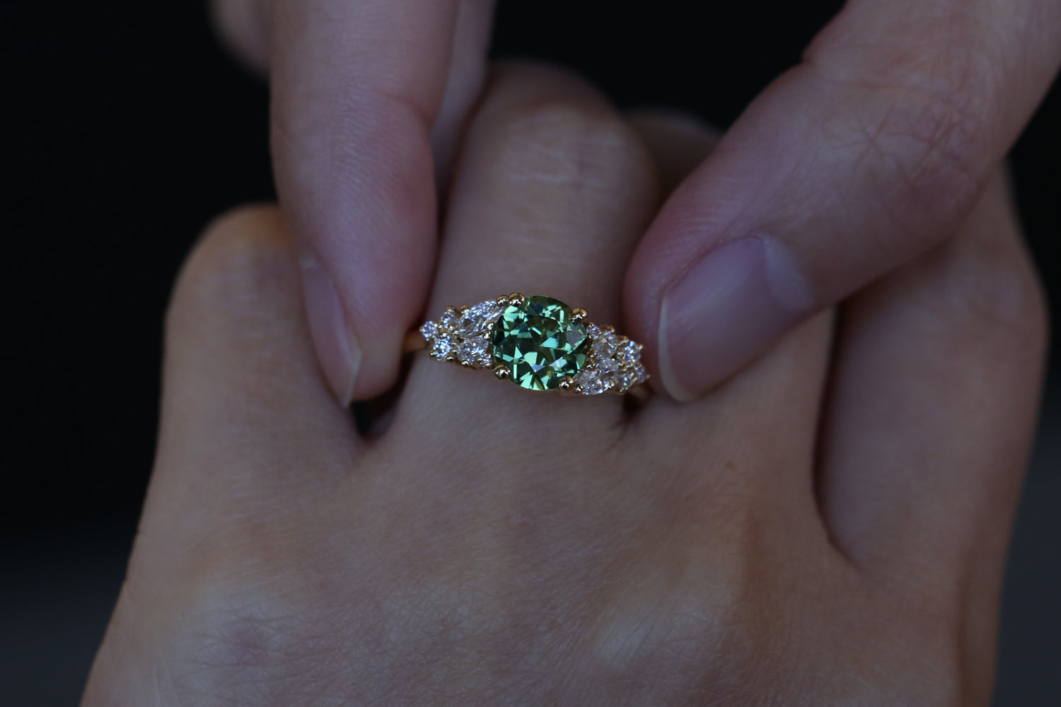 Close-up of a hand wearing a ring with a green Australian sapphire on a dark background