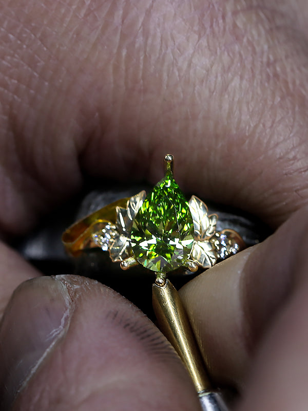 Gold ring with a green diamond held between fingers